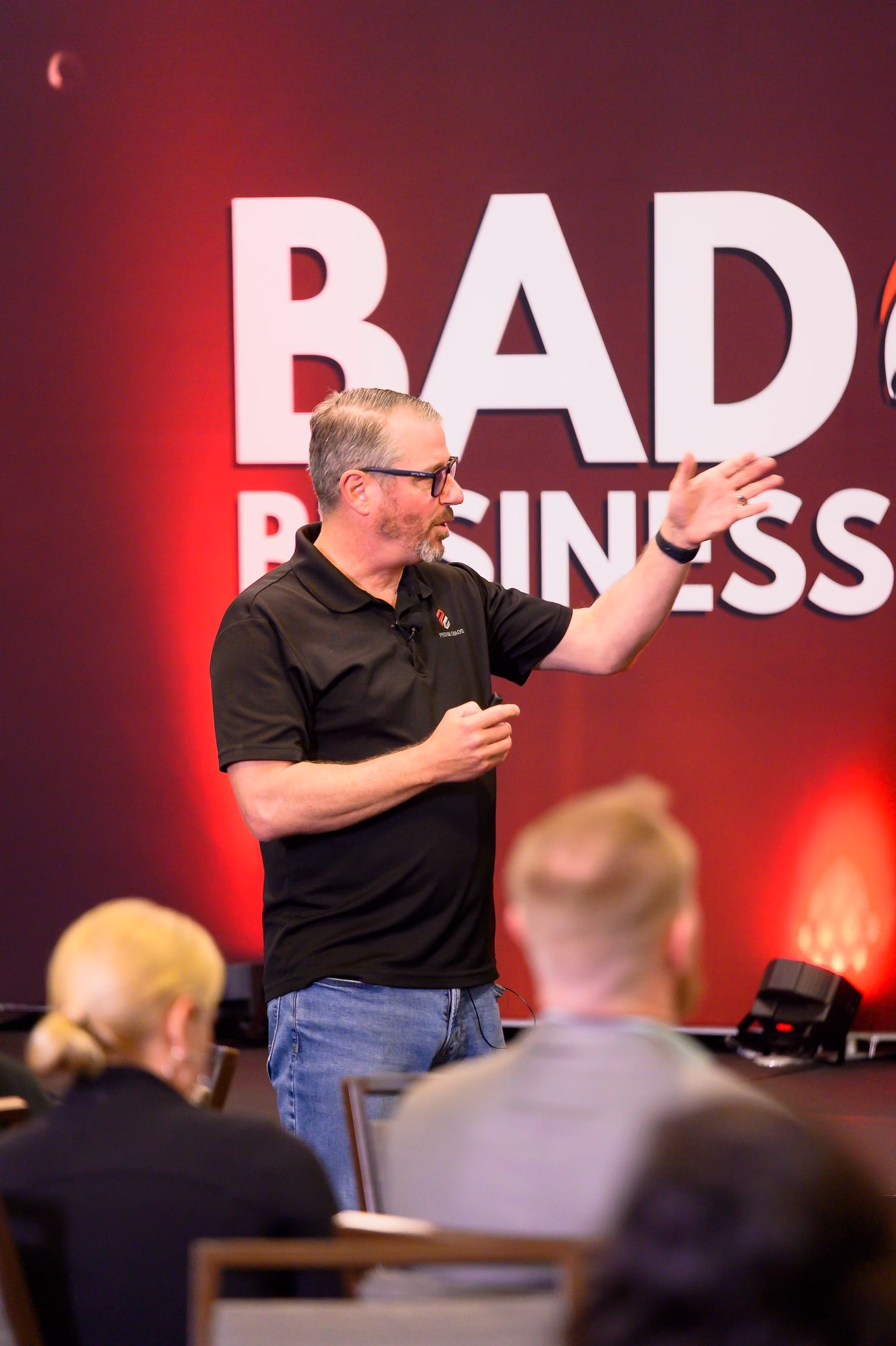 Jerry Macnamara speaking on stage in front of the Badass Business Summit wall